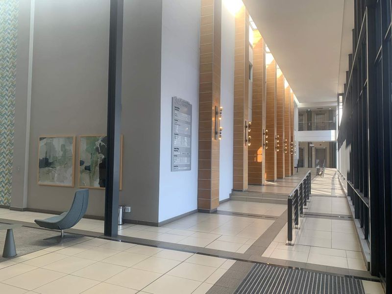 A spacious, modern office building lobby featuring high ceilings, tiled floors, large glass windows, and professional directory signage.