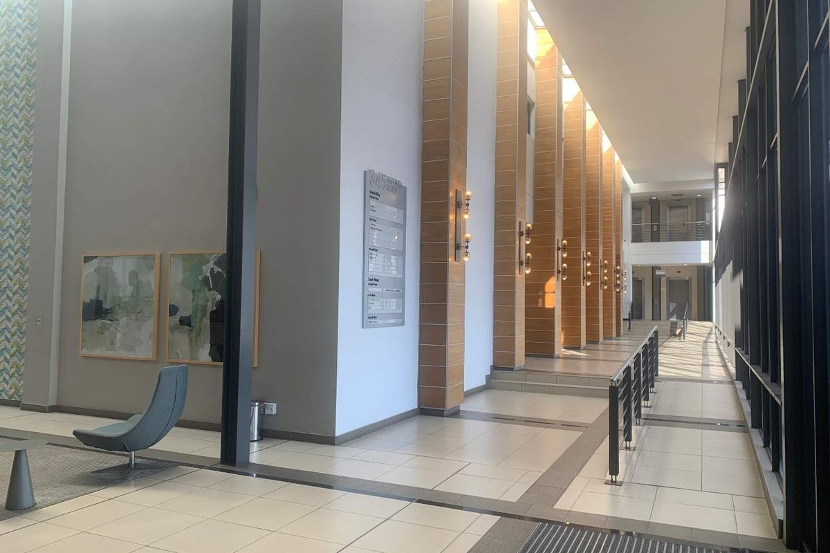 A spacious, modern office building lobby featuring high ceilings, tiled floors, large glass windows, and professional directory signage.