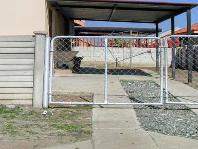 Front exterior view of the townhouse featuring a metal carport, gated entrance, and concrete driveway area.