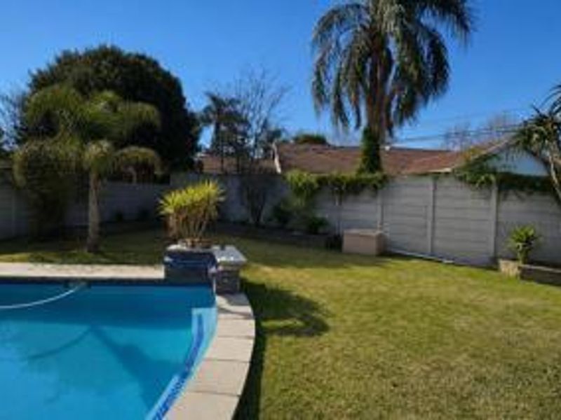 A well-maintained backyard featuring a swimming pool, established garden, and secure precast concrete boundary walling.