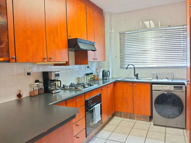 Functional kitchen featuring wood-look cabinetry, dark countertops, gas hob, built-in oven, and tiled finishes with ample natural light.