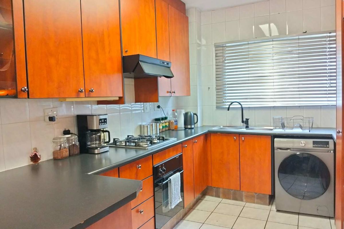 Functional kitchen featuring wood-look cabinetry, dark countertops, gas hob, built-in oven, and tiled finishes with ample natural light.