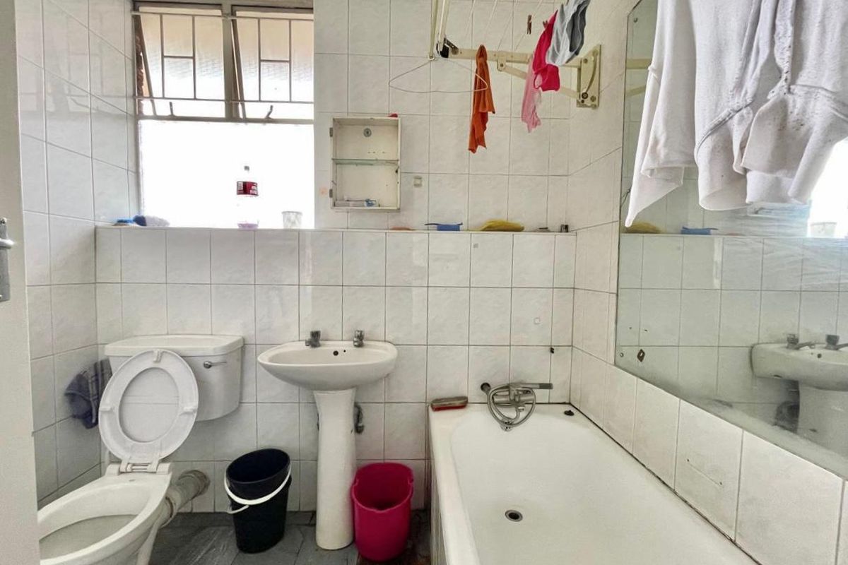 A dated bathroom featuring a standard bathtub, pedestal basin, and toilet with full-height wall tiling and a large wall-mounted mirror.