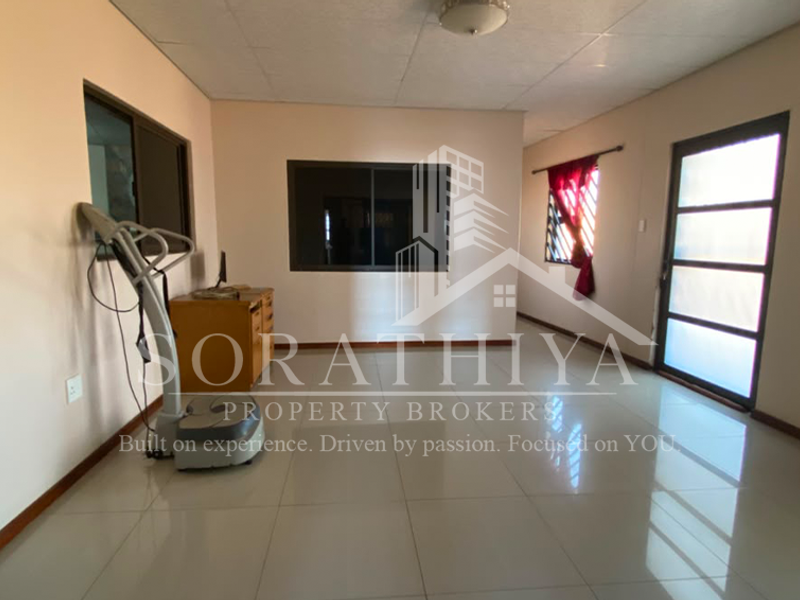 A spacious living area featuring neutral walls, large tiled flooring, and natural light through aluminium-framed windows and a glass panel door.