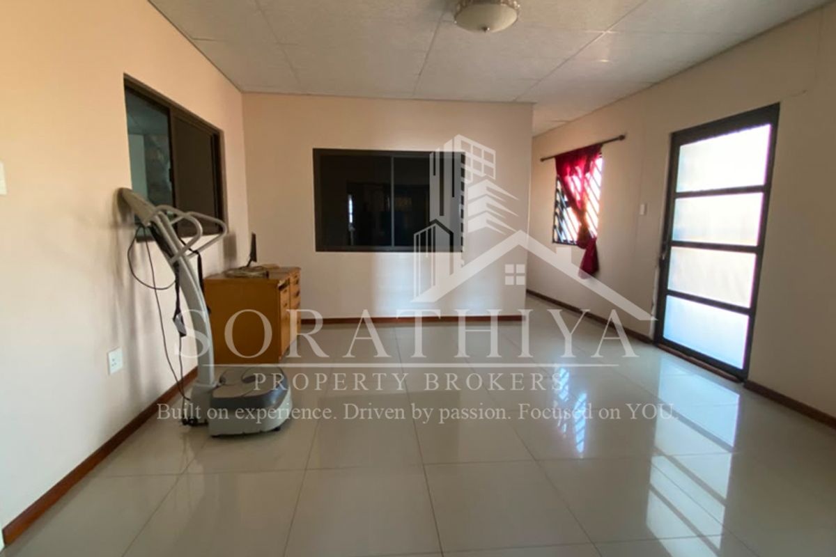 A spacious living area featuring neutral walls, large tiled flooring, and natural light through aluminium-framed windows and a glass panel door.