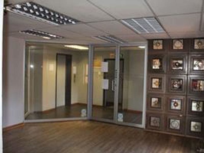 An empty office space featuring glass partitions, suspended ceilings with integrated lighting, and decorative wall paneling with wood-look laminate flooring.