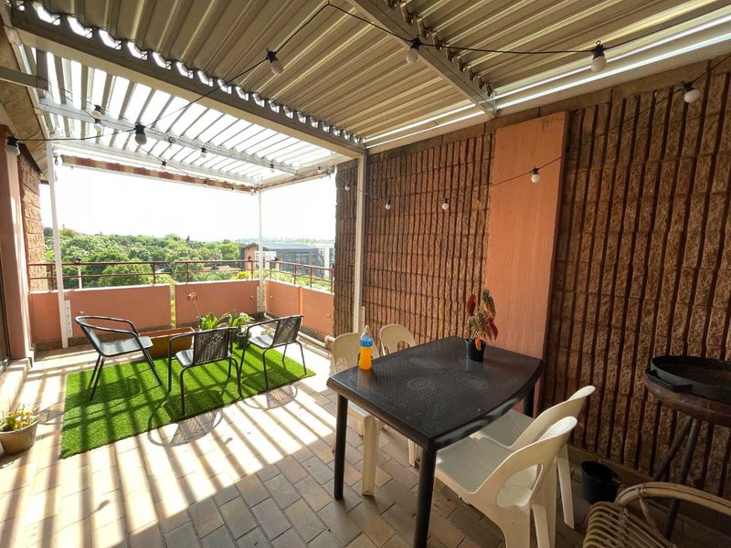 A covered balcony featuring a corrugated metal roof, brick wall finishes, and paved flooring, offering an outdoor space with elevated views.