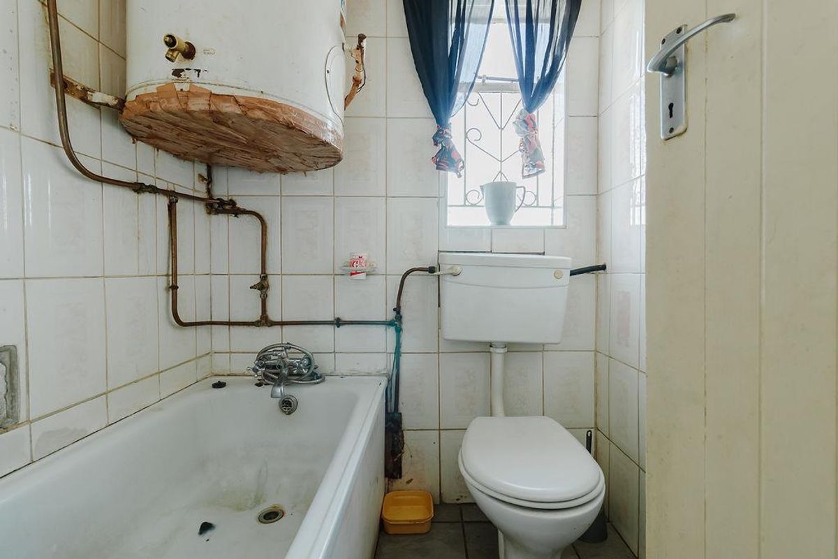 A compact bathroom featuring a bathtub, toilet, and wall-mounted water heater, requiring significant maintenance and cosmetic updates to improve its condition.