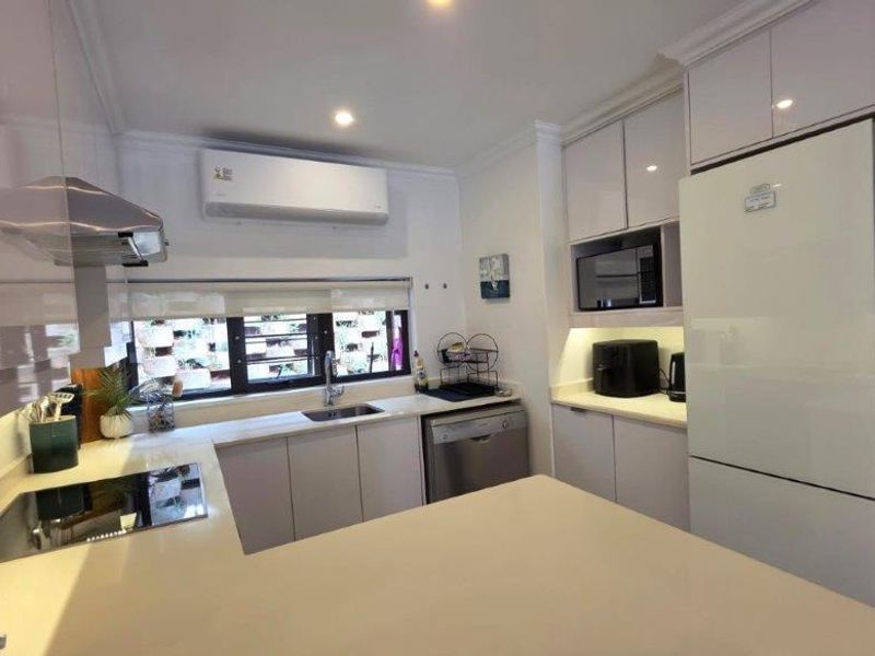 Modern kitchen featuring sleek white cabinetry, stone countertops, integrated appliances, and a split-system air conditioner, offering a clean and functional culinary space.