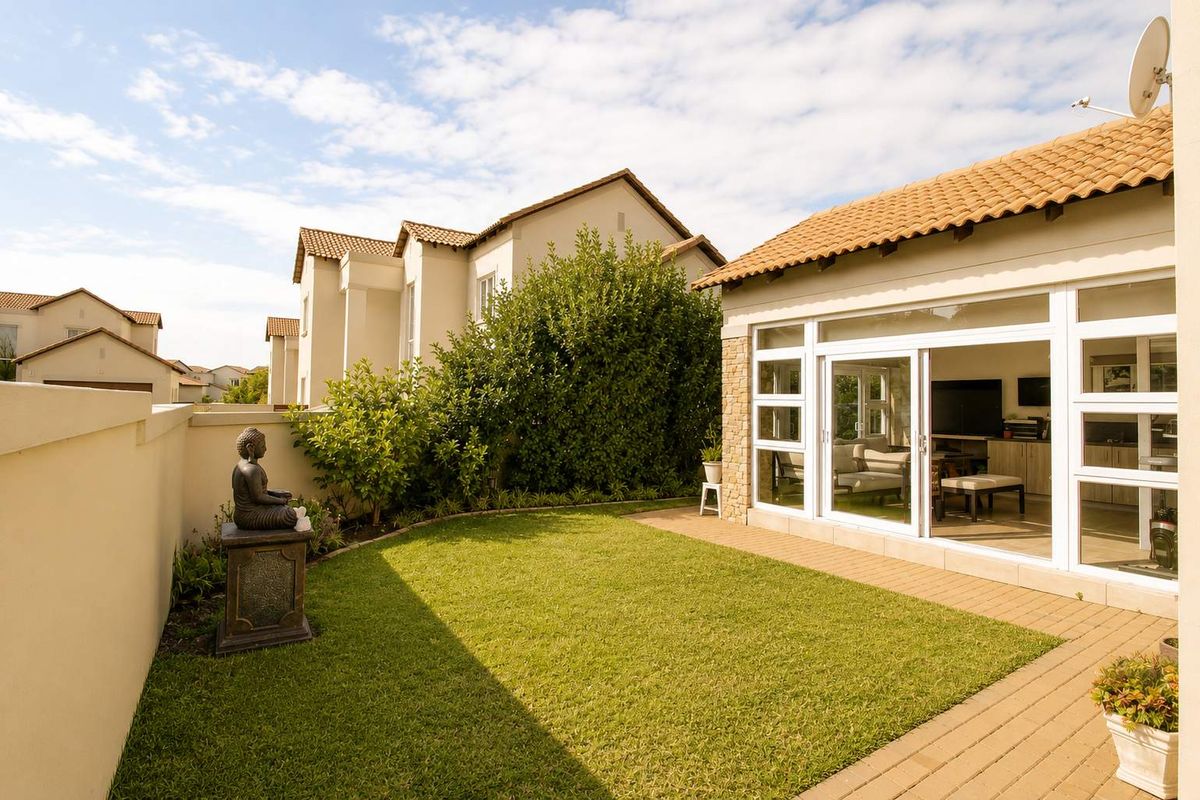 A well-maintained rear garden featuring a manicured lawn, paved patio area, and direct access to the interior living space through large sliding glass doors.
