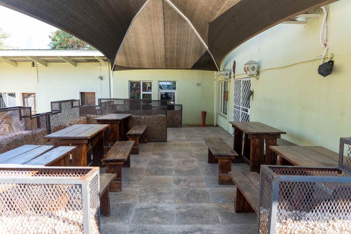 Outdoor patio area featuring tiled flooring, a large overhead shade sail, and wall-mounted lighting, providing a functional space for guests.