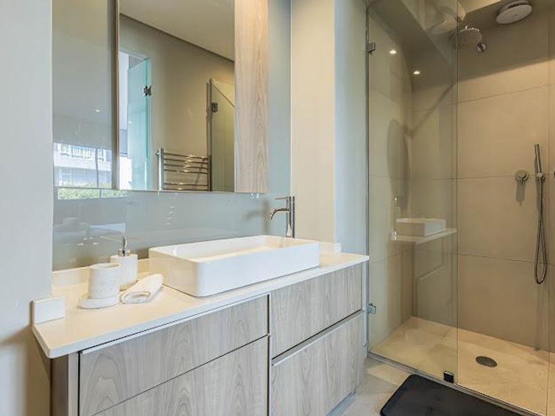 Modern bathroom featuring a sleek vanity with countertop basin, large wall mirror, and a spacious walk-in shower with glass enclosure and premium fixtures.