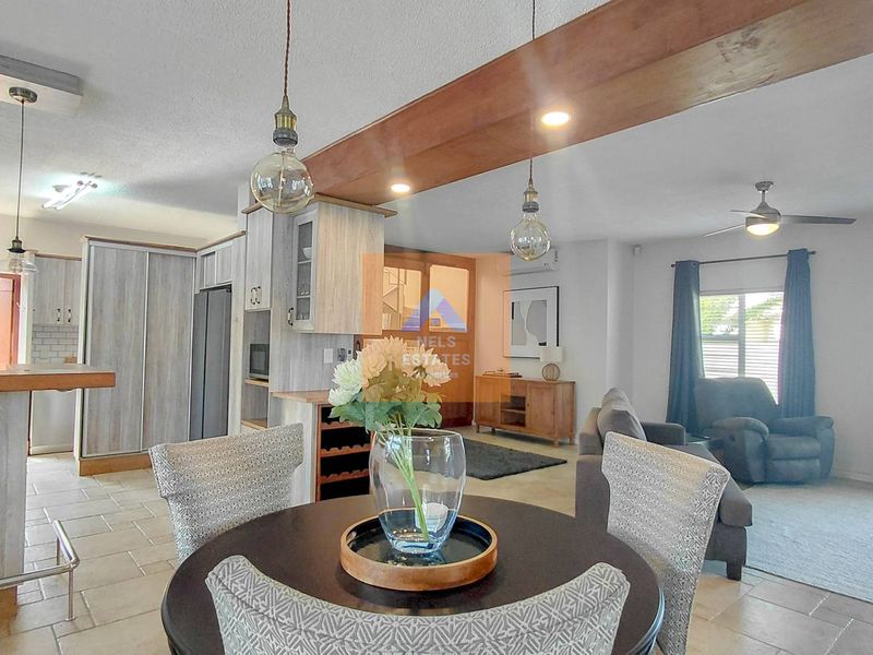 Spacious open-plan living and kitchen area featuring tiled floors, an exposed timber ceiling beam, and modern pendant lighting.
