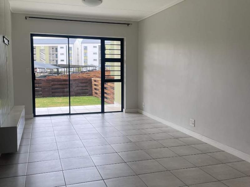 A bright, empty living room featuring neutral tiled flooring and a large sliding glass door providing access to the outdoor area.