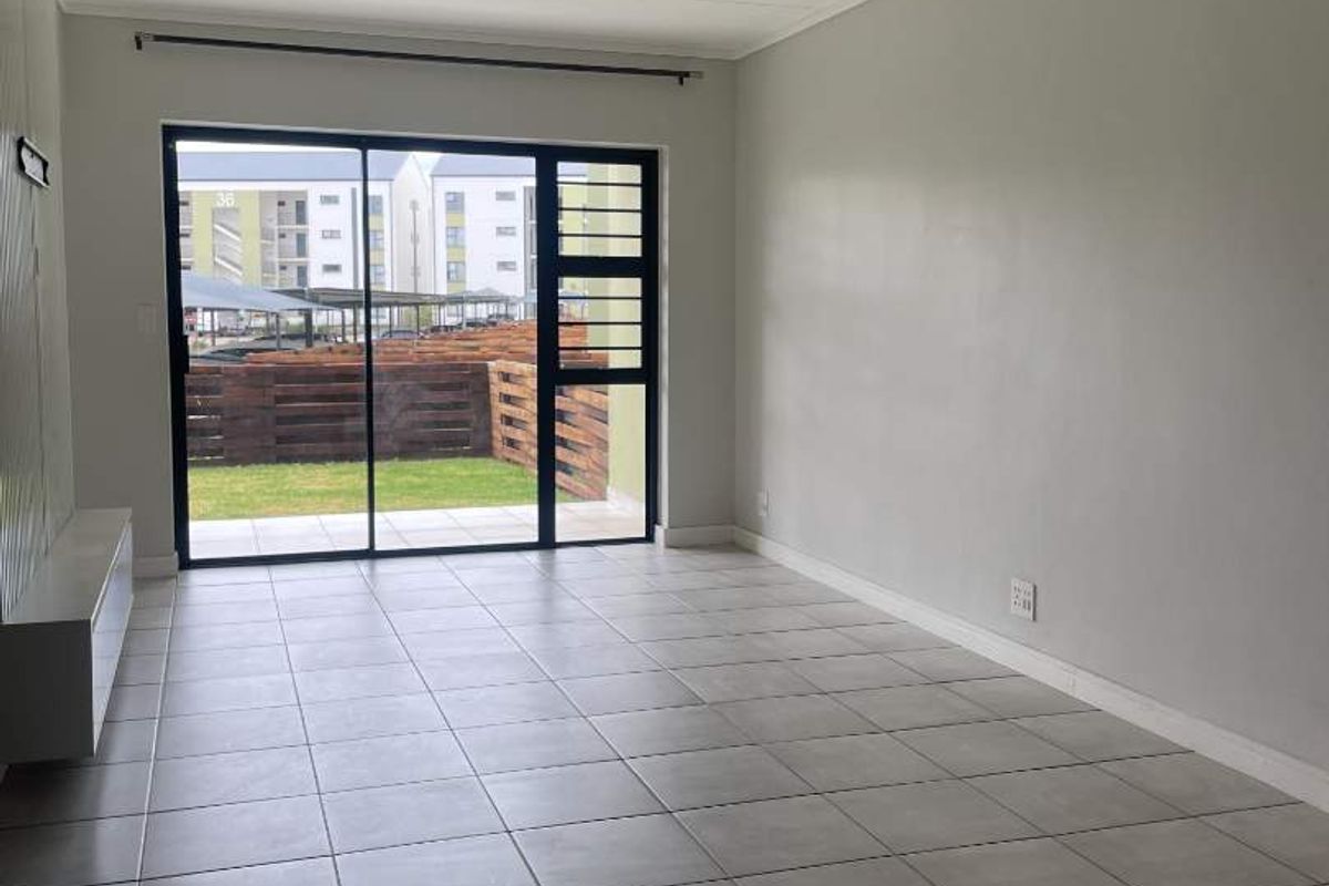 A bright, empty living room featuring neutral tiled flooring and a large sliding glass door providing access to the outdoor area.