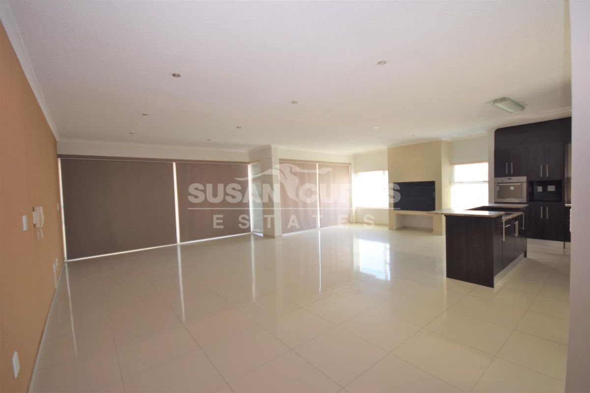 Spacious open-plan living area featuring polished tile flooring, recessed lighting, and a modern kitchen with dark cabinetry and built-in oven.