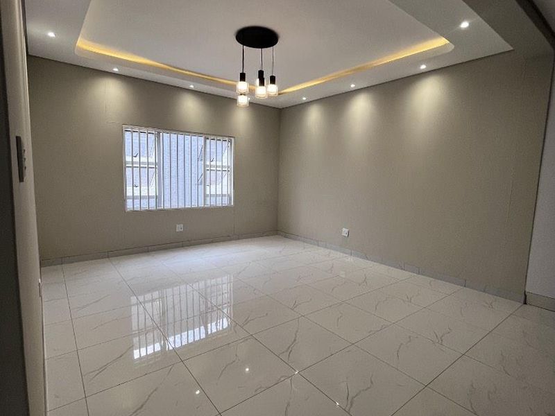A bright, empty living room featuring modern porcelain floor tiles, a decorative recessed ceiling with cove lighting, and integrated downlights.