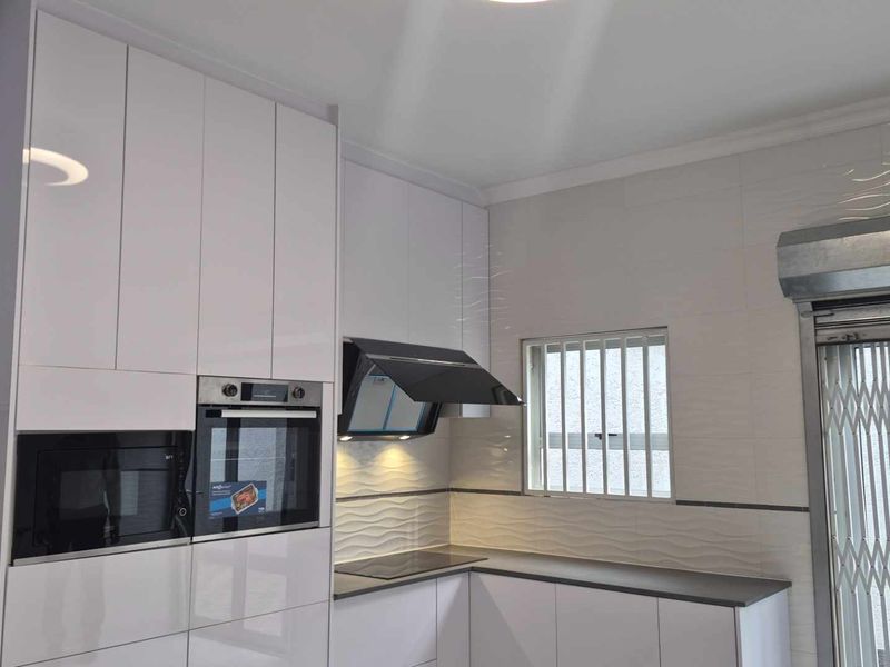 Modern kitchen featuring high-gloss white cabinetry, integrated oven and microwave, sleek extractor fan, and a textured tiled backsplash.