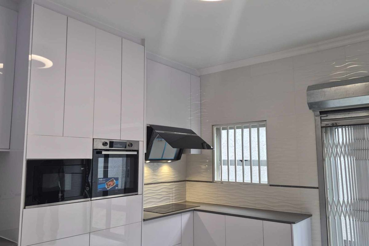 Modern kitchen featuring high-gloss white cabinetry, integrated oven and microwave, sleek extractor fan, and a textured tiled backsplash.