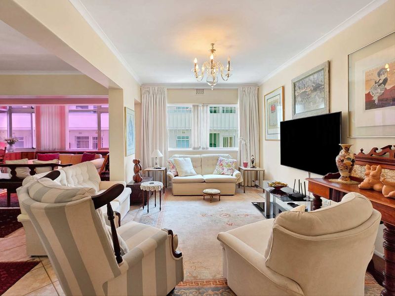 Spacious open-plan living area featuring tiled flooring, decorative coving, and a central chandelier, with an adjacent secondary living space visible.