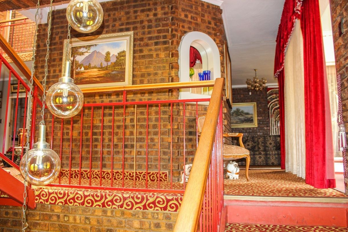 Interior view of a multi-level living area featuring exposed brick walls, a red metal staircase railing, and a built-in arched wall niche.