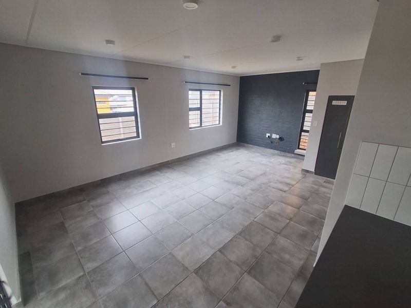 A spacious, modern open-plan living area featuring neutral grey tiled flooring, recessed lighting, and a striking dark accent wall.