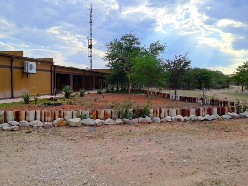 Rear exterior view of the farm building featuring a covered patio, retaining wall, and surrounding landscape with a communication tower in the background.