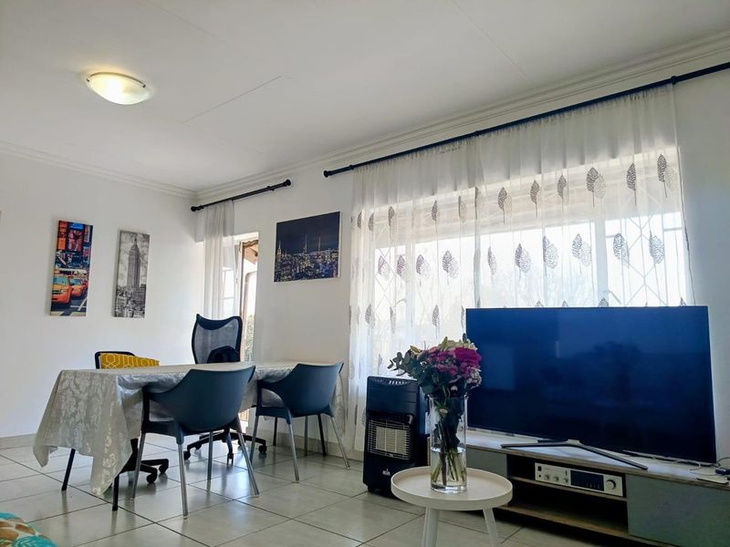 A bright living room featuring tiled flooring, large windows with curtain rods, and a ceiling-mounted light fixture.