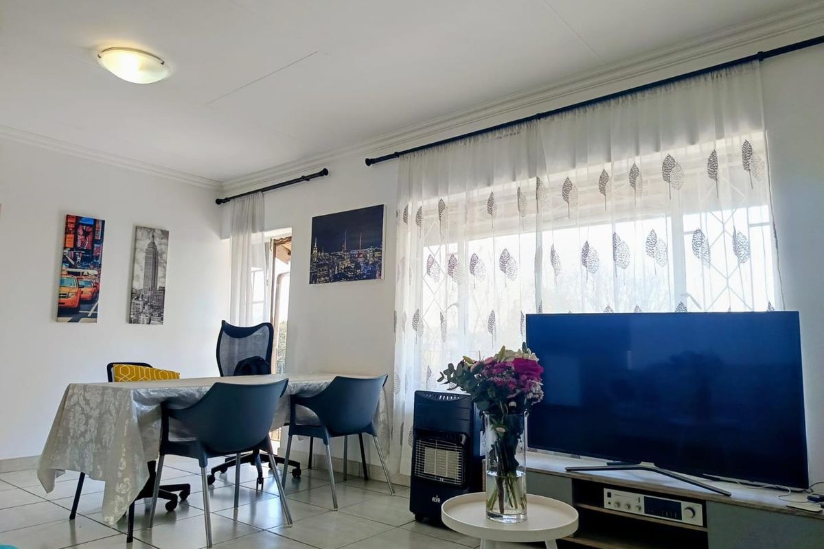 A bright living room featuring tiled flooring, large windows with curtain rods, and a ceiling-mounted light fixture.