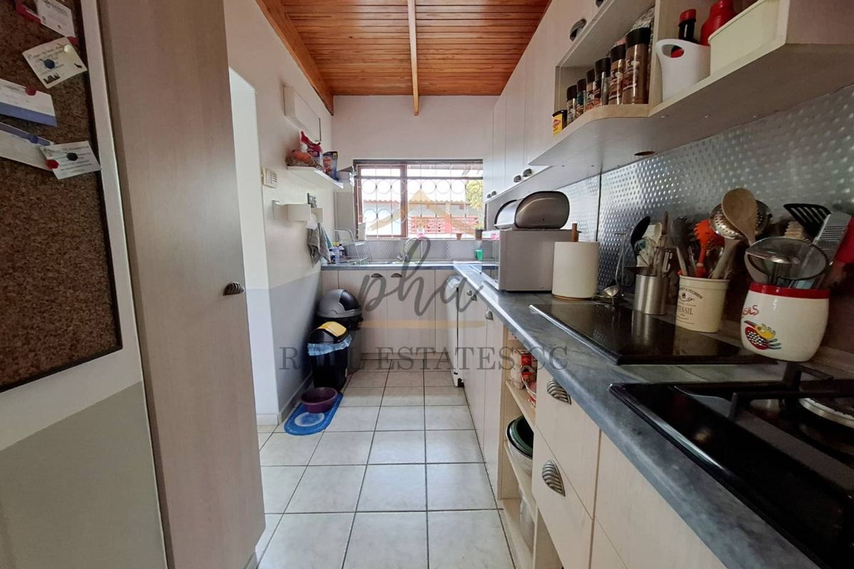 A functional galley-style kitchen featuring tiled flooring, timber-paneled ceiling, built-in cabinetry, and a stainless steel splashback.