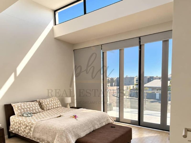 Bright and modern bedroom featuring high ceilings with clerestory windows, sleek laminate flooring, and large sliding glass doors leading to an outdoor balcony.