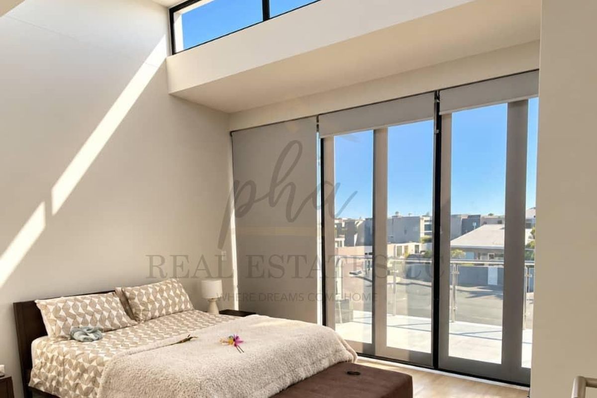 Bright and modern bedroom featuring high ceilings with clerestory windows, sleek laminate flooring, and large sliding glass doors leading to an outdoor balcony.