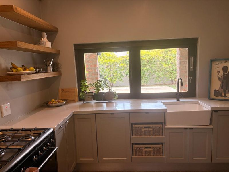 A well-appointed kitchen featuring shaker-style cabinetry, stone countertops, an apron sink, and floating timber shelving with a built-in gas stove.