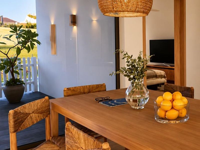 A bright dining area featuring modern wood flooring, a woven pendant light, and seamless access to an outdoor patio through large sliding glass doors.