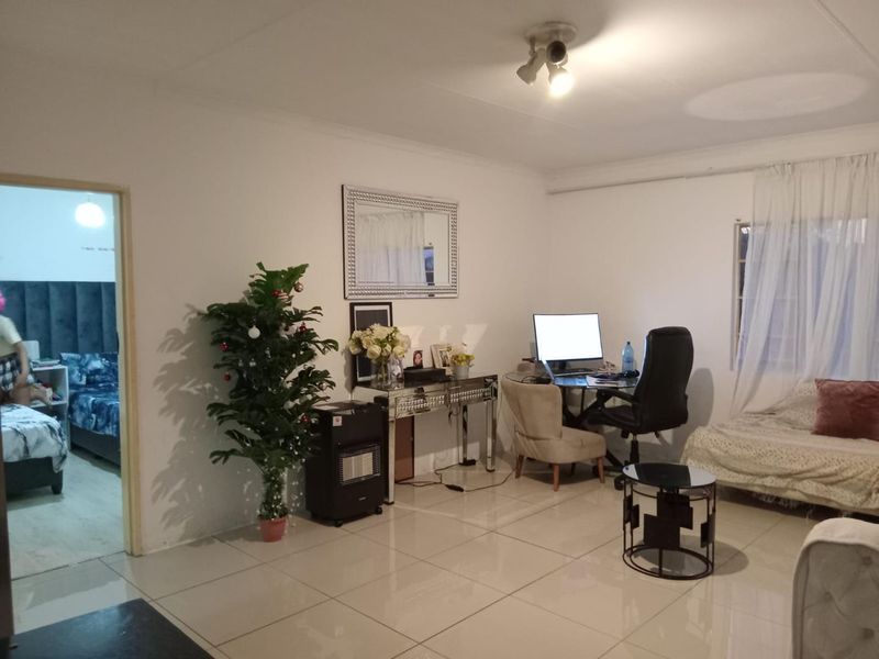 A living room area featuring tiled flooring and neutral walls, providing a functional space with access to an adjacent bedroom.