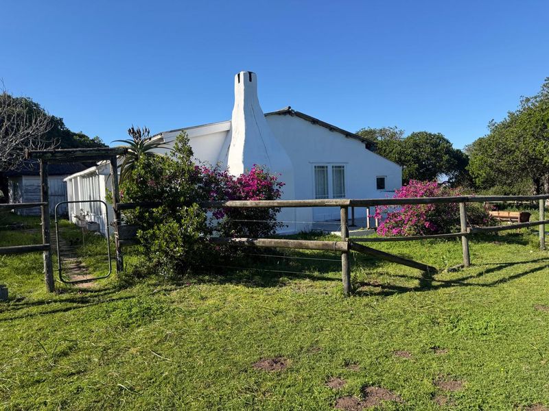 Rear view of a white farmhouse featuring a prominent chimney, double glass doors, and a surrounding timber post and rail fence.