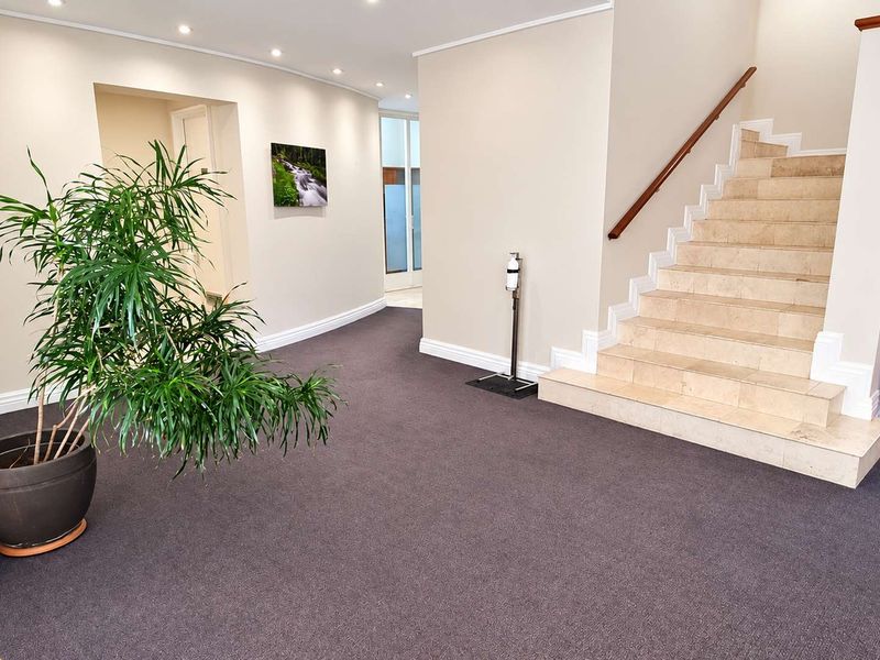 Spacious office entrance foyer featuring neutral walls, dark carpeting, and a stone staircase with a wooden handrail.