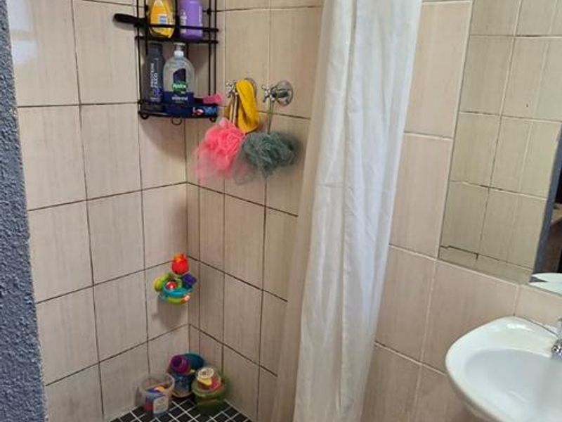 A functional bathroom featuring a tiled shower enclosure with a rainfall shower head and a classic pedestal basin.