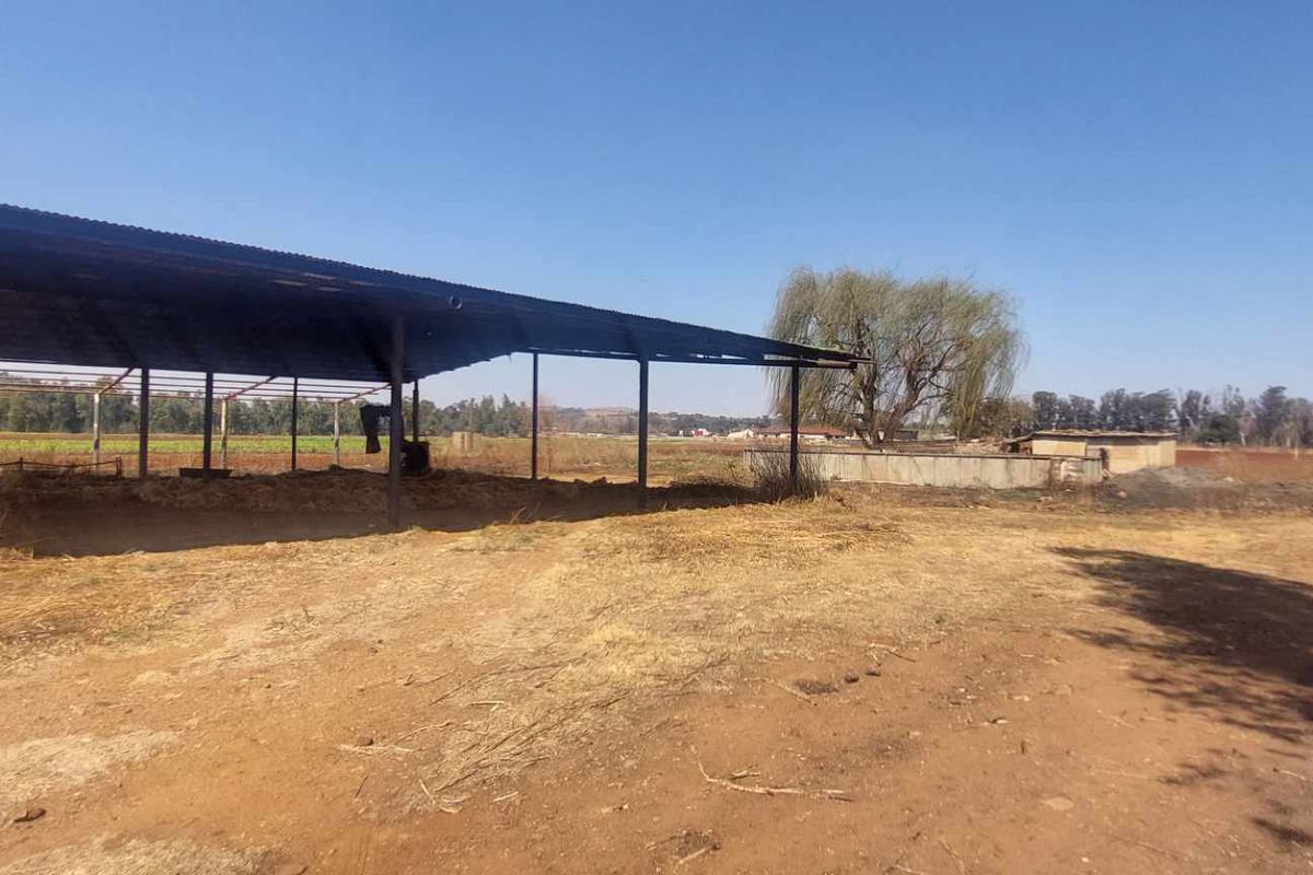 An open-sided agricultural shed structure situated on a large rural farm plot with expansive landscape views.