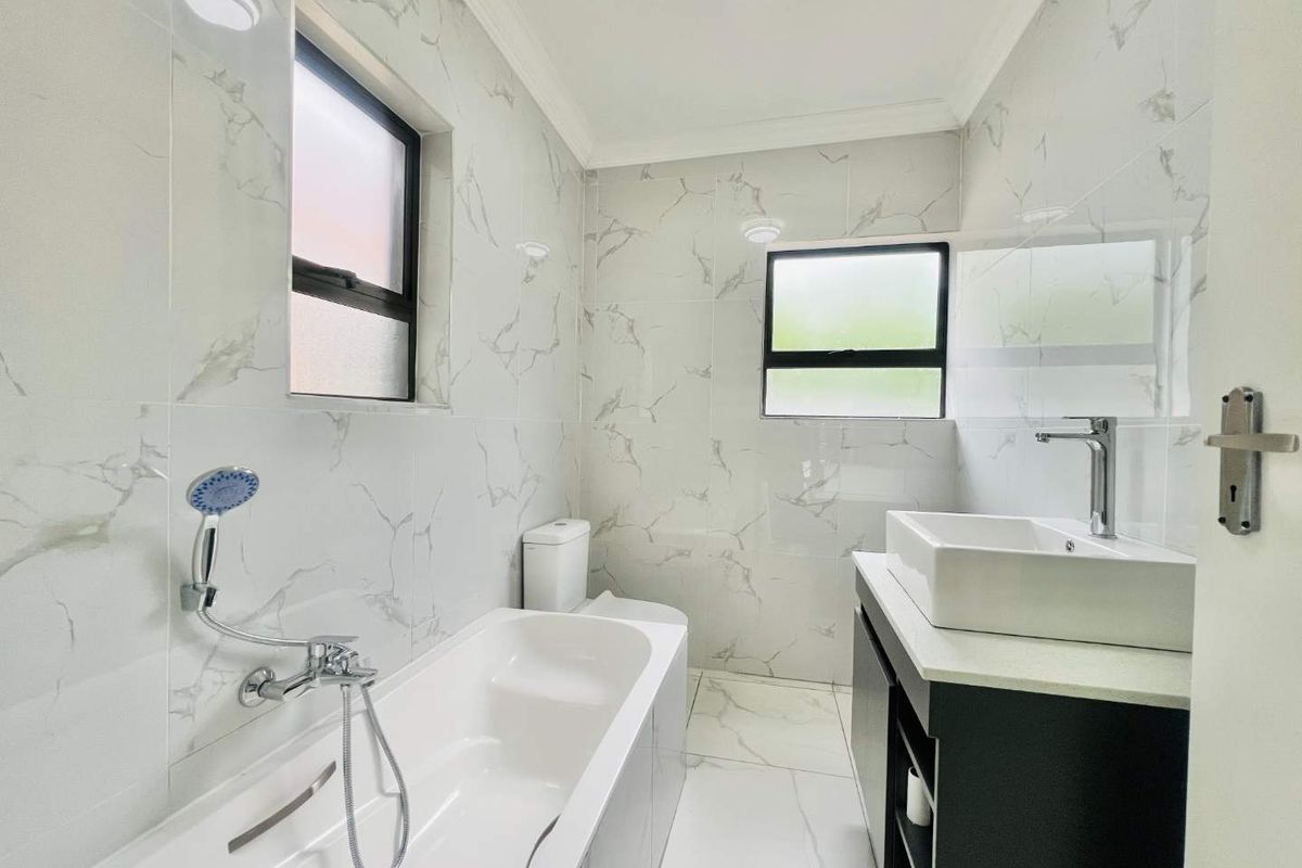 Modern bathroom featuring marble-look wall and floor tiles, a contemporary vanity with a vessel sink, and a built-in bathtub with a handheld shower fixture.