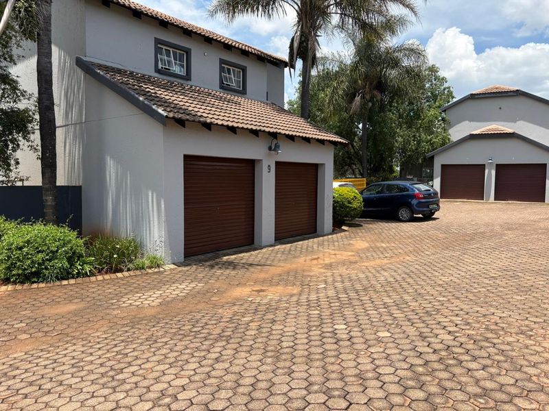 Front view of a cluster home featuring a double garage with roll-up doors, tiled roof, and a paved driveway.