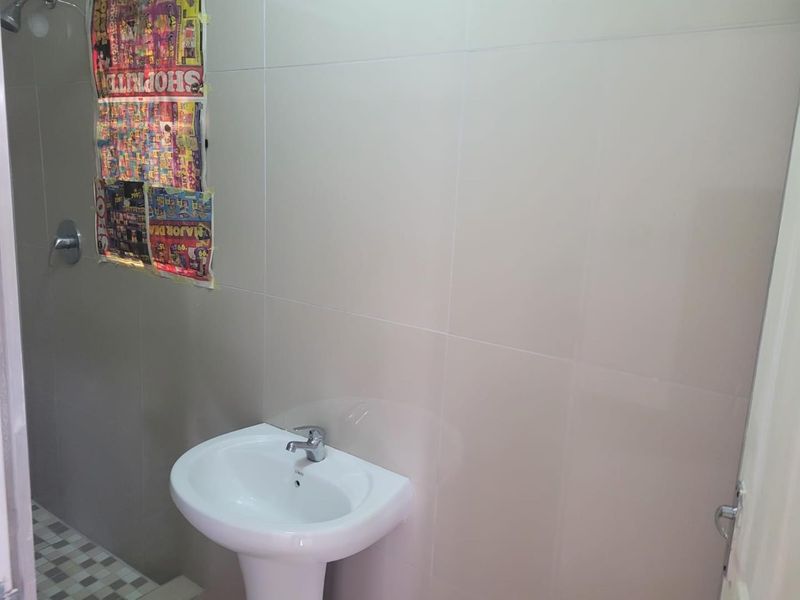 A functional bathroom featuring a pedestal washbasin, chrome fixtures, and neutral wall tiling with mosaic floor accents.