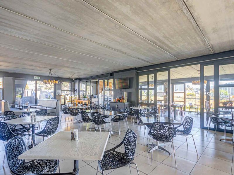 Spacious open-plan dining area featuring an exposed concrete ceiling, tiled flooring, and extensive glass sliding doors providing ample natural light and outdoor access.