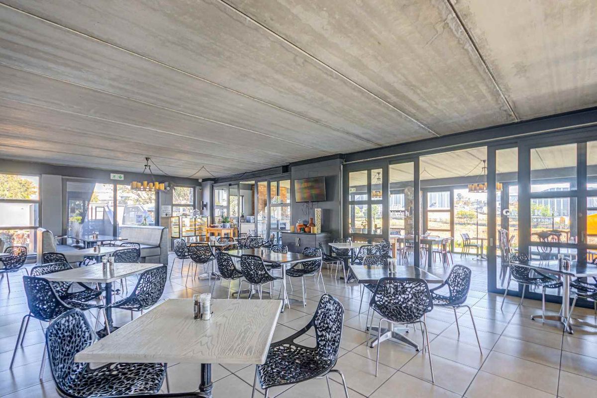 Spacious open-plan dining area featuring an exposed concrete ceiling, tiled flooring, and extensive glass sliding doors providing ample natural light and outdoor access.