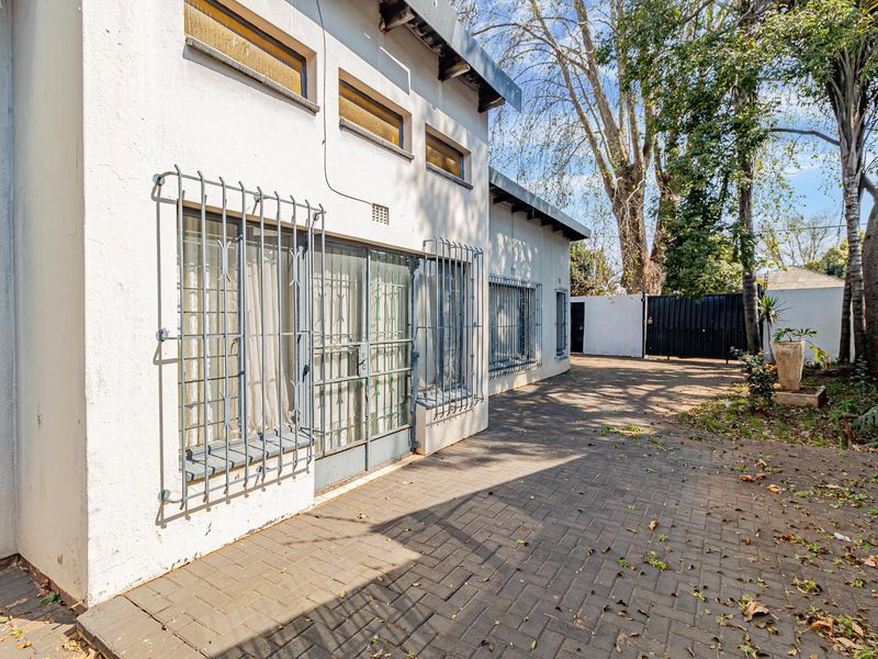 Rear exterior view of the property featuring a paved patio area, security bars on windows, and a secure perimeter wall with a metal gate.