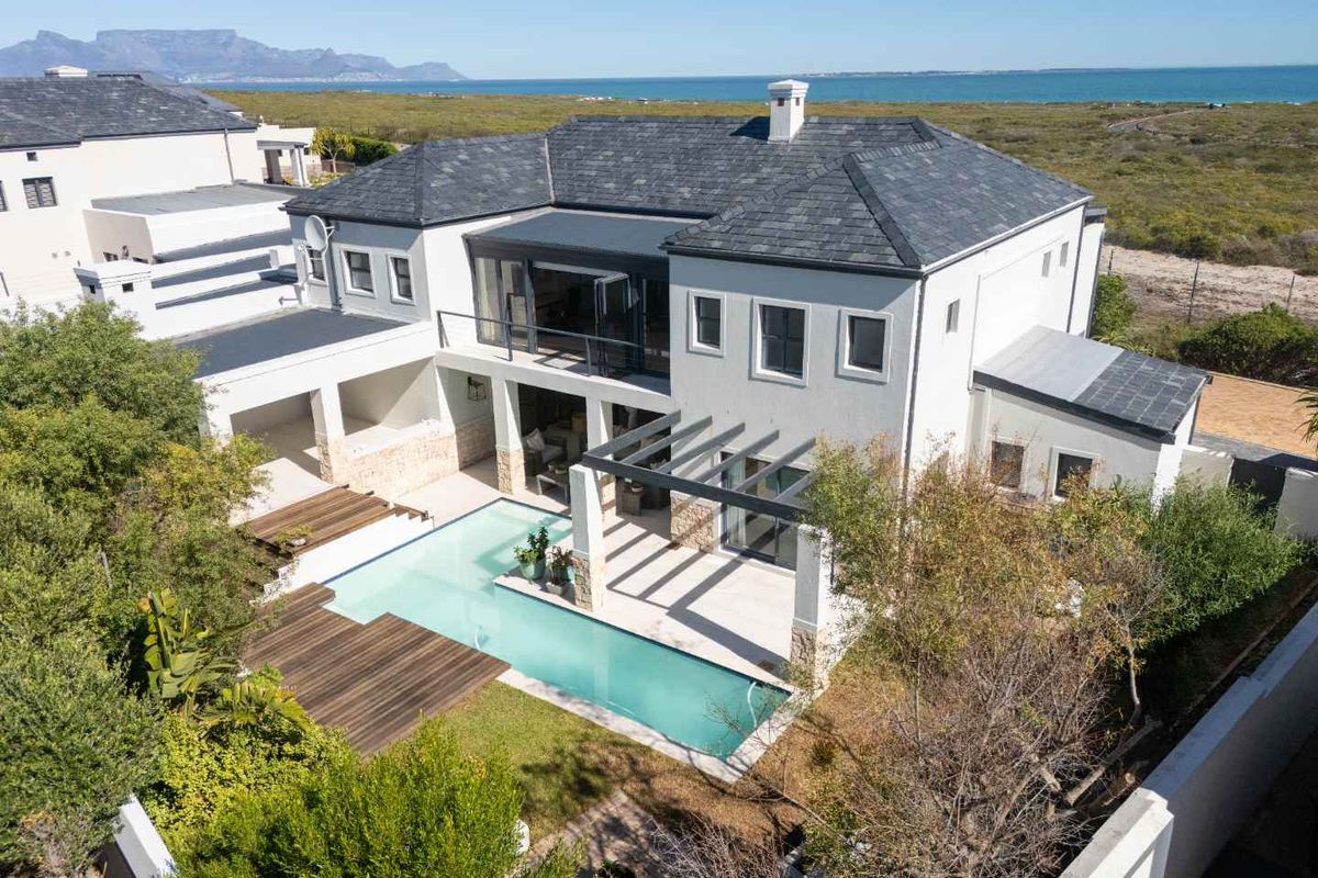 Aerial view of a modern two-story residence featuring a swimming pool, timber decking, covered patio, and a slate-tiled roof with coastal views.