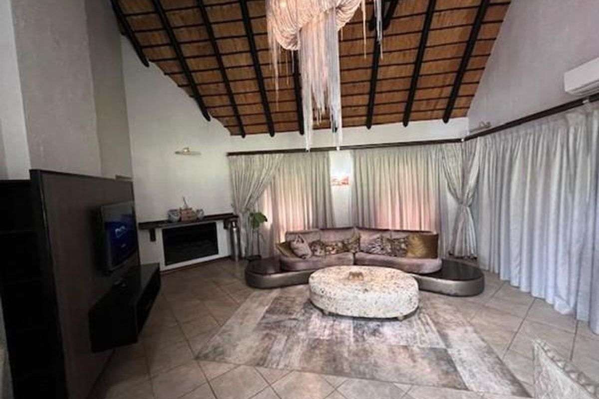 Spacious living room featuring a high vaulted thatched ceiling, tiled flooring, a built-in fireplace, and large windows with floor-to-ceiling curtains.