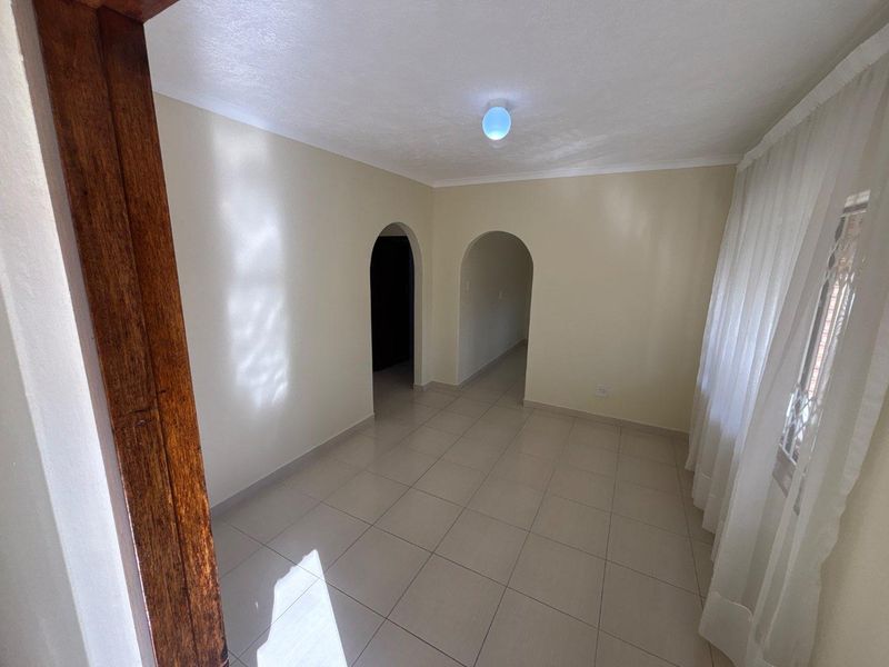 A bright, empty living area featuring neutral ceramic floor tiles, clean walls, and distinctive arched doorways leading to adjacent spaces.