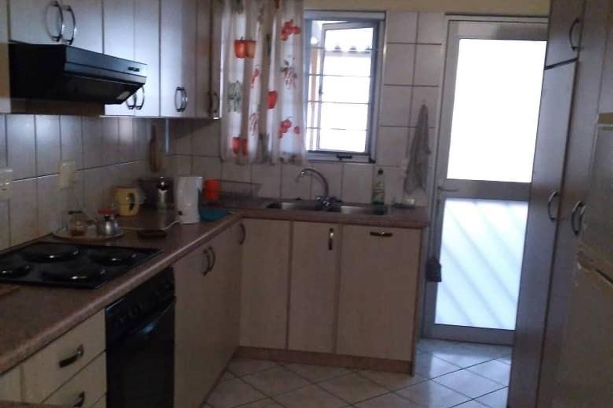 A functional kitchen featuring built-in cabinetry, a hob, an oven, an extractor fan, and a tiled floor with direct access to the exterior.
