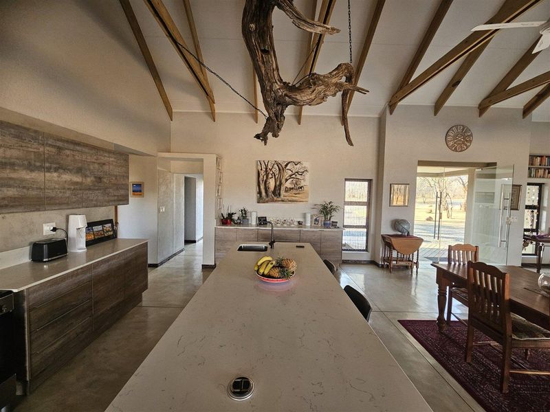 Spacious open-plan kitchen and living area featuring a large central island, polished concrete floors, and striking exposed timber rafters under a high vaulted ceiling.